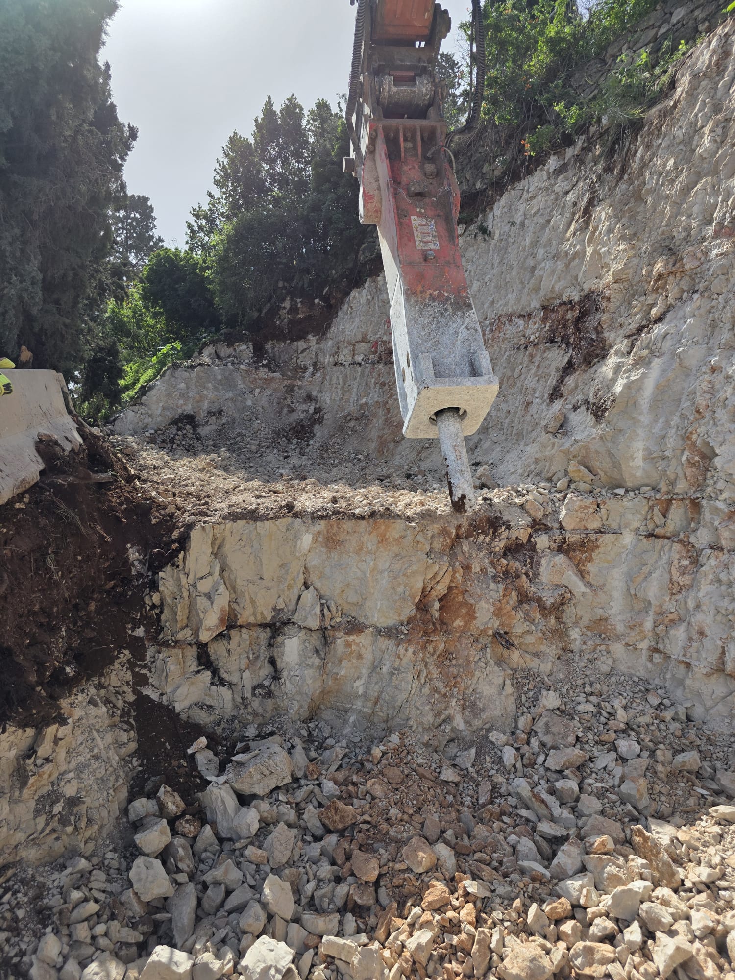 מפרץ סלעים הידראולי מפרק מדרון סלעי, יוצר הריסות וחושף שכבות של אדמה ואבן.